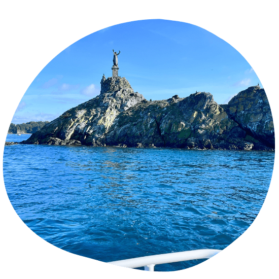 Statue atop rocky island surrounded by blue sea under clear sky.