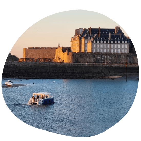 Boat near historic stone building by a calm waterfront at sunset.