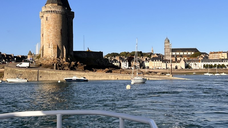 View of a historic tower and buildings by water, with boats and clear sky.