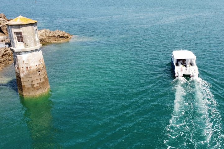 Boat sailing near lighthouse tower on rocky coast.