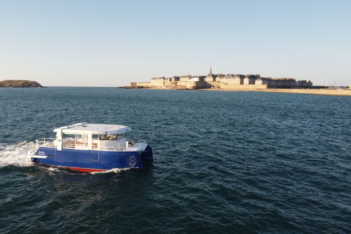 Blue boat on the sea near a coastal town under a clear sky.