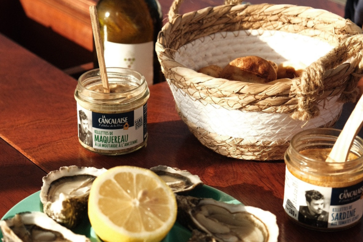 Jars of spread, bread basket, oysters, lemon on a table.