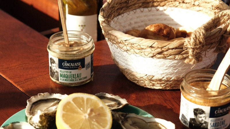 Jars of spread, bread basket, oysters, lemon on a table.