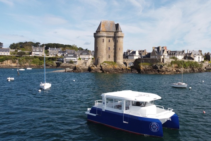 Small blue and white boat on water near coastal town with a medieval tower.