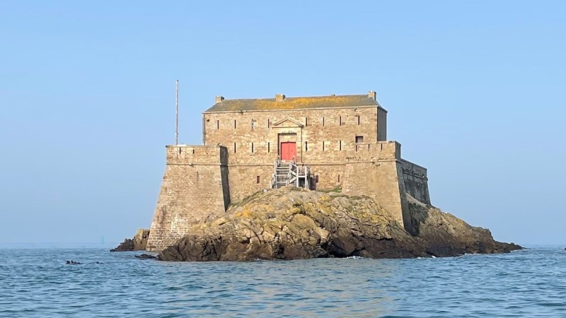 Stone fortress on rocky island surrounded by water under blue sky.