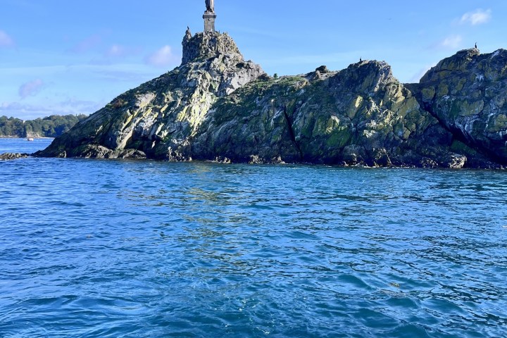 Small rocky island with a statue on top, surrounded by blue water.