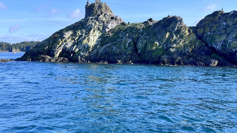 Small rocky island with a statue on top, surrounded by blue water.