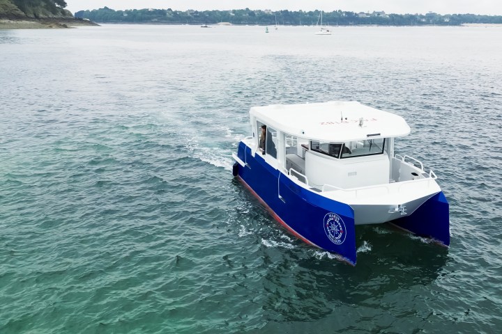 Small white and blue catamaran cruising on calm waters with distant shore.