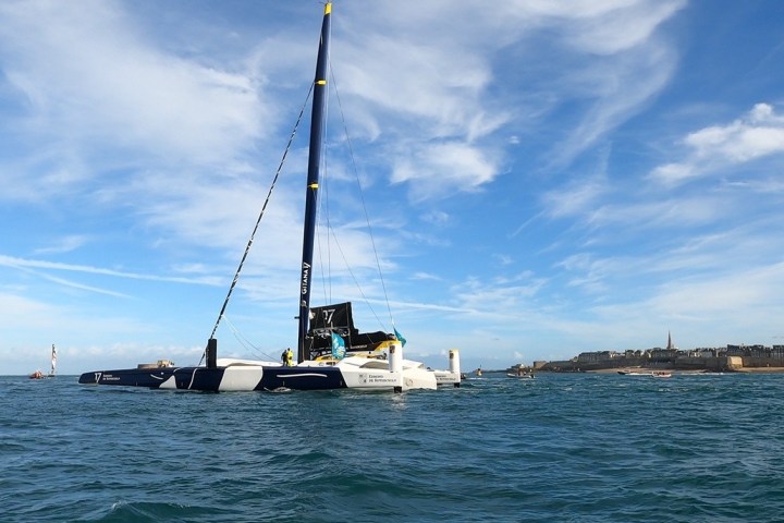 Sailboat on blue water under a partly cloudy sky with distant shoreline.
