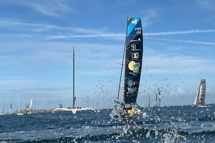 Sailboats racing on open water with splashing waves in the foreground.