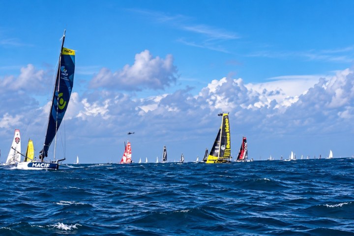 Multiple sailboats racing on a blue ocean under a partly cloudy sky.