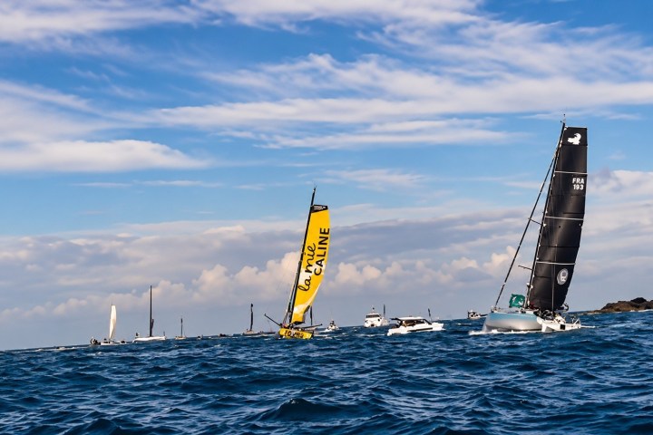 Sailboats racing near a lighthouse under a cloudy sky.